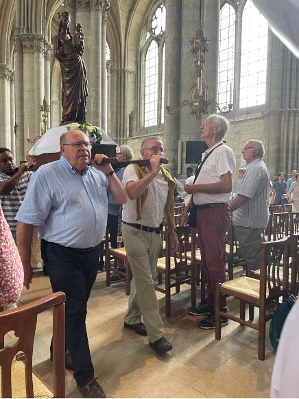People of various ages inside the cathedral for a service. Three men can be seen carrying a heavy box on their shoulders up the aisle.