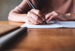 Closeup image of a woman writing on notebook on wooden table.