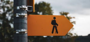 Photograph of an orange sign with a drawing of a man walking carrying a backpack and holding a walking stick