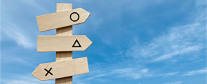 Wooden sign with three arrows. One pointing right with a circle, one also pointing with a triangle and the third pointing left with a cross. The background is a blue sky with whispy white clouds.